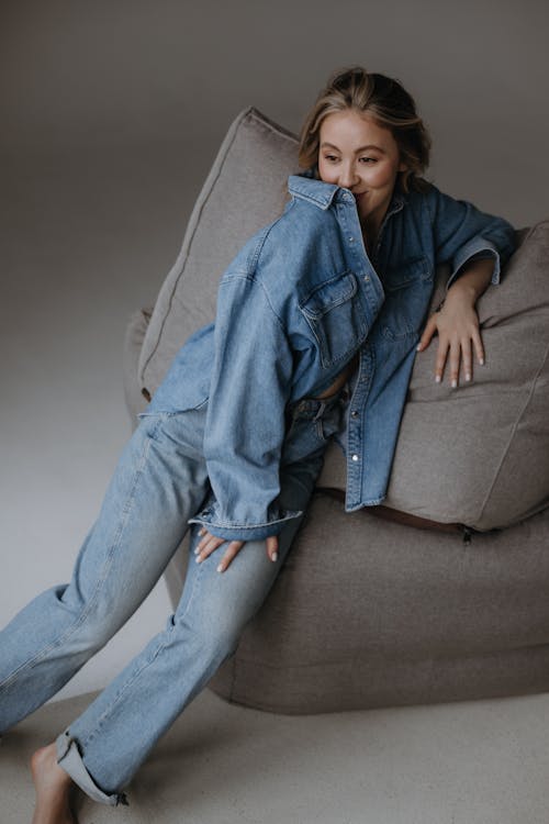A woman in jeans and a denim jacket sitting on a couch