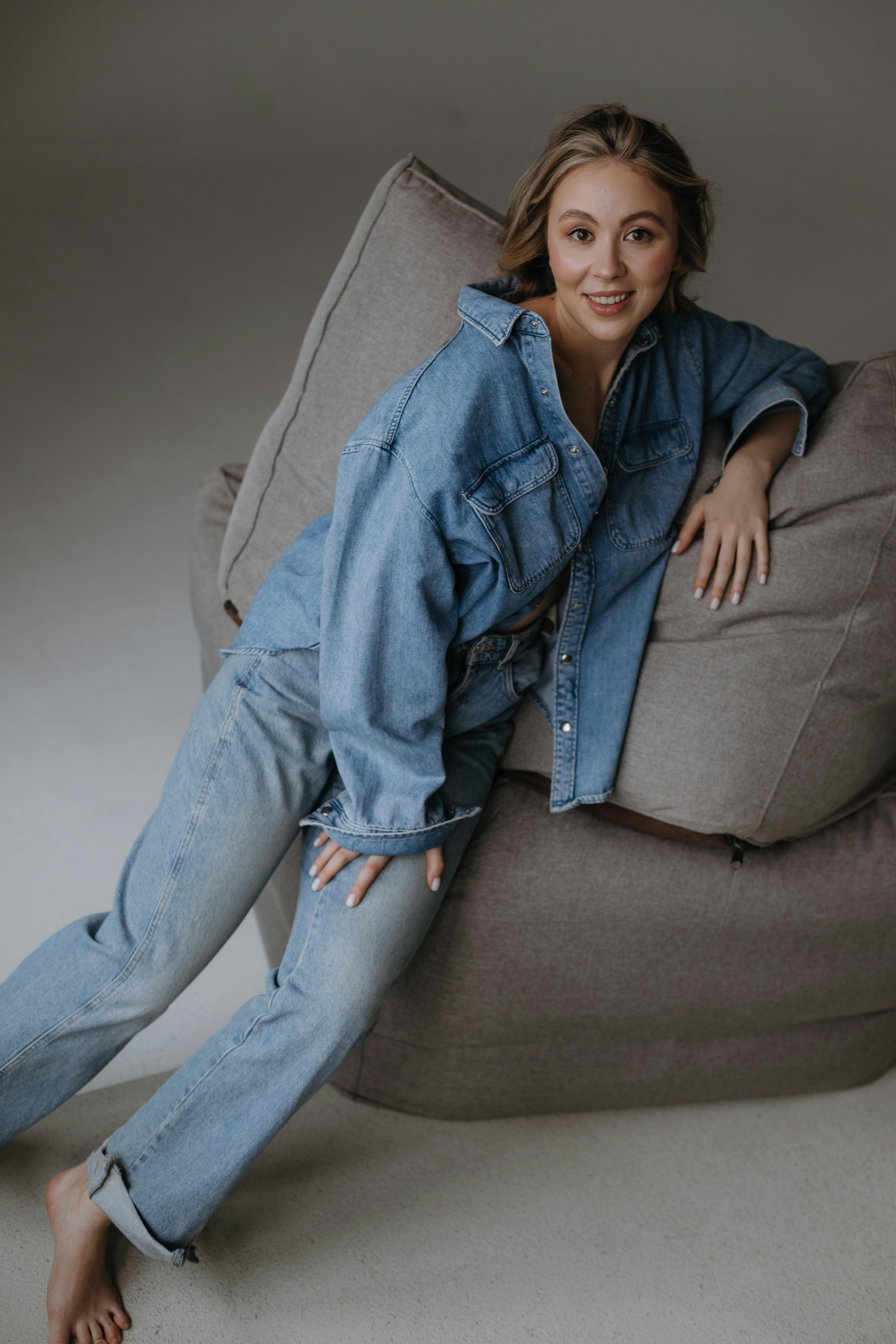 Stylish woman in a denim outfit leaning on a pillow in a studio setting.
