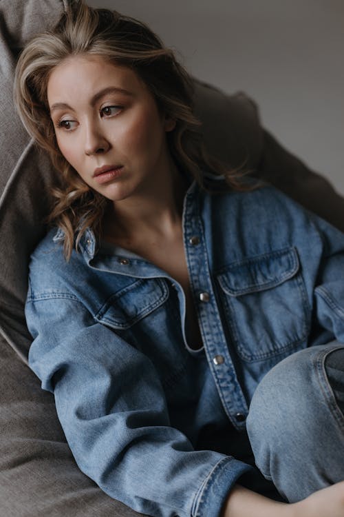 A woman in a denim shirt and jeans sitting on a couch
