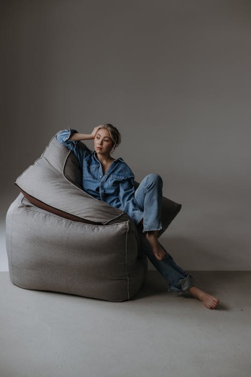 Studio Shot of a Woman in Denim Outfit Sitting on Large Cushions 