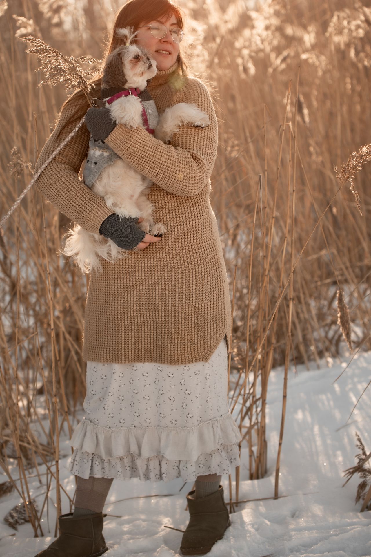 Woman in a knit sweater dress and boots standing in the snow