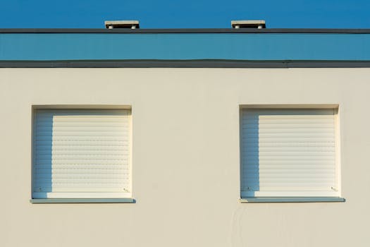 Two closed shutter windows on a modern building façade against a clear sky.