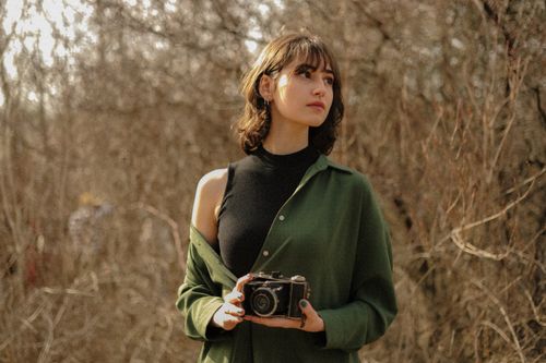 Free A young woman holding a vintage camera in an autumn forest setting. Stock Photo