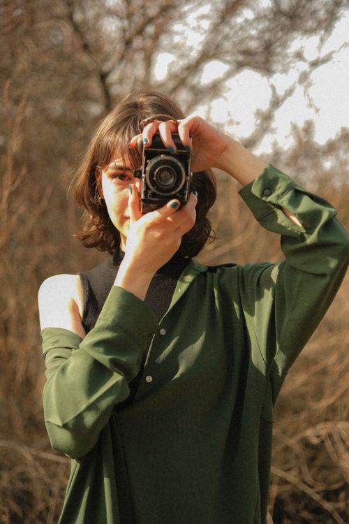 Free A young woman in a green outfit holding a vintage camera in an outdoor autumn setting. Stock Photo