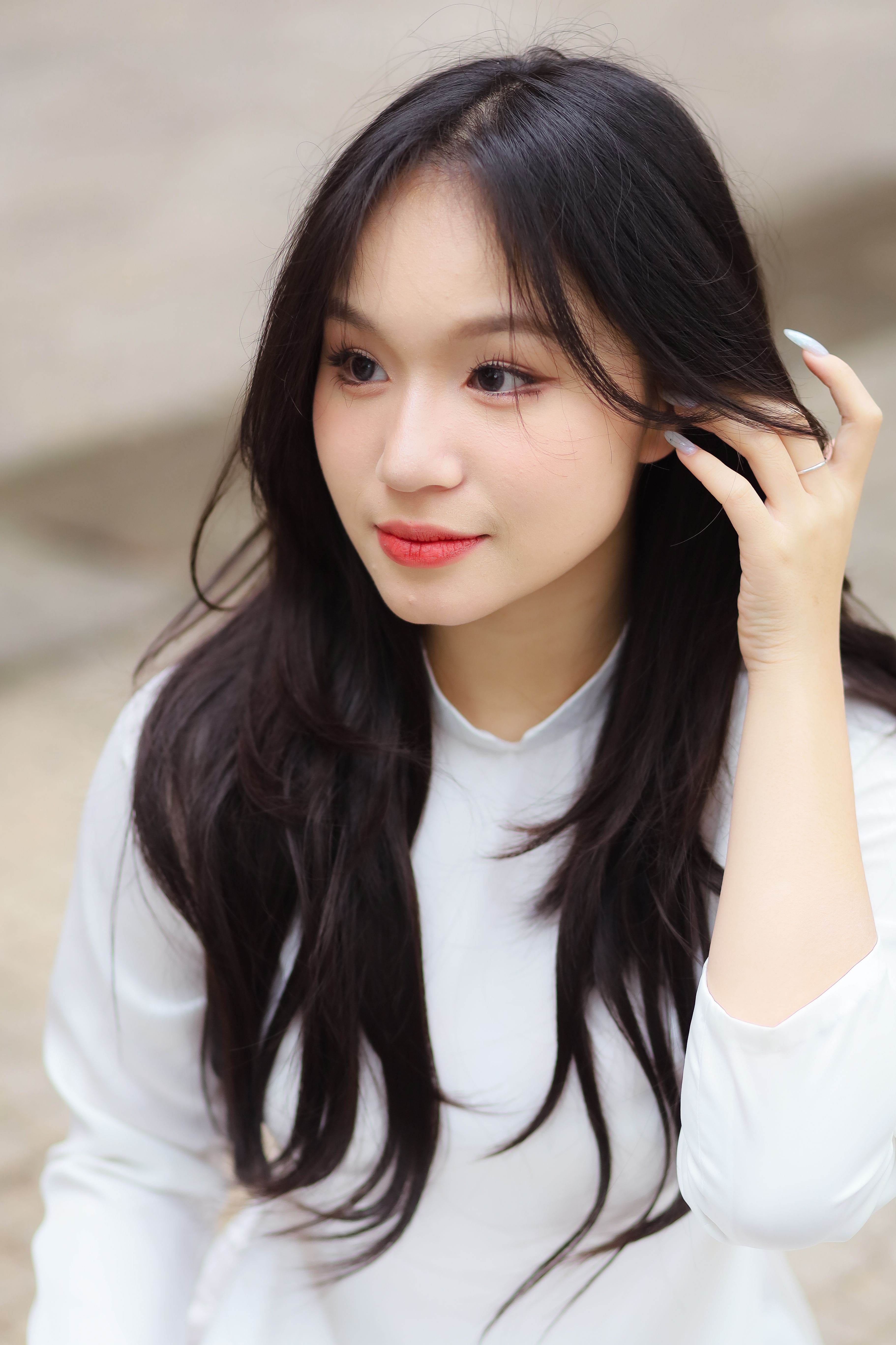 Portrait of a young woman in a white tunic with long dark hair. Outdoors, natural light.