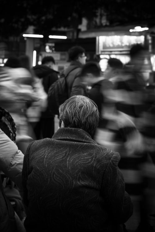 Free Black and white photo of an elderly woman sitting in a bustling city street. Stock Photo