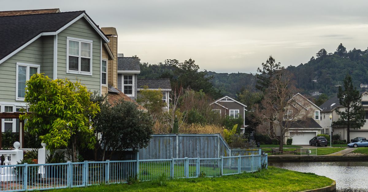 Quaint residential suburb with homes by a serene canal under a cloudy summer sky.