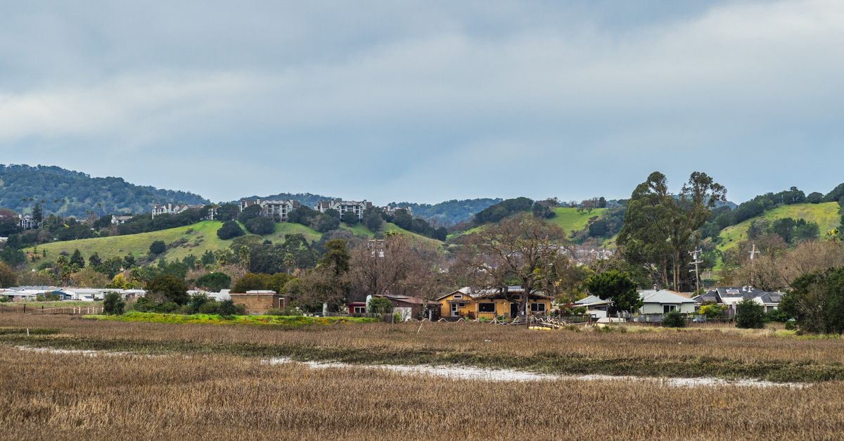 Picturesque rural scene depicting hills, village houses, and lush fields under a cloudy sky.