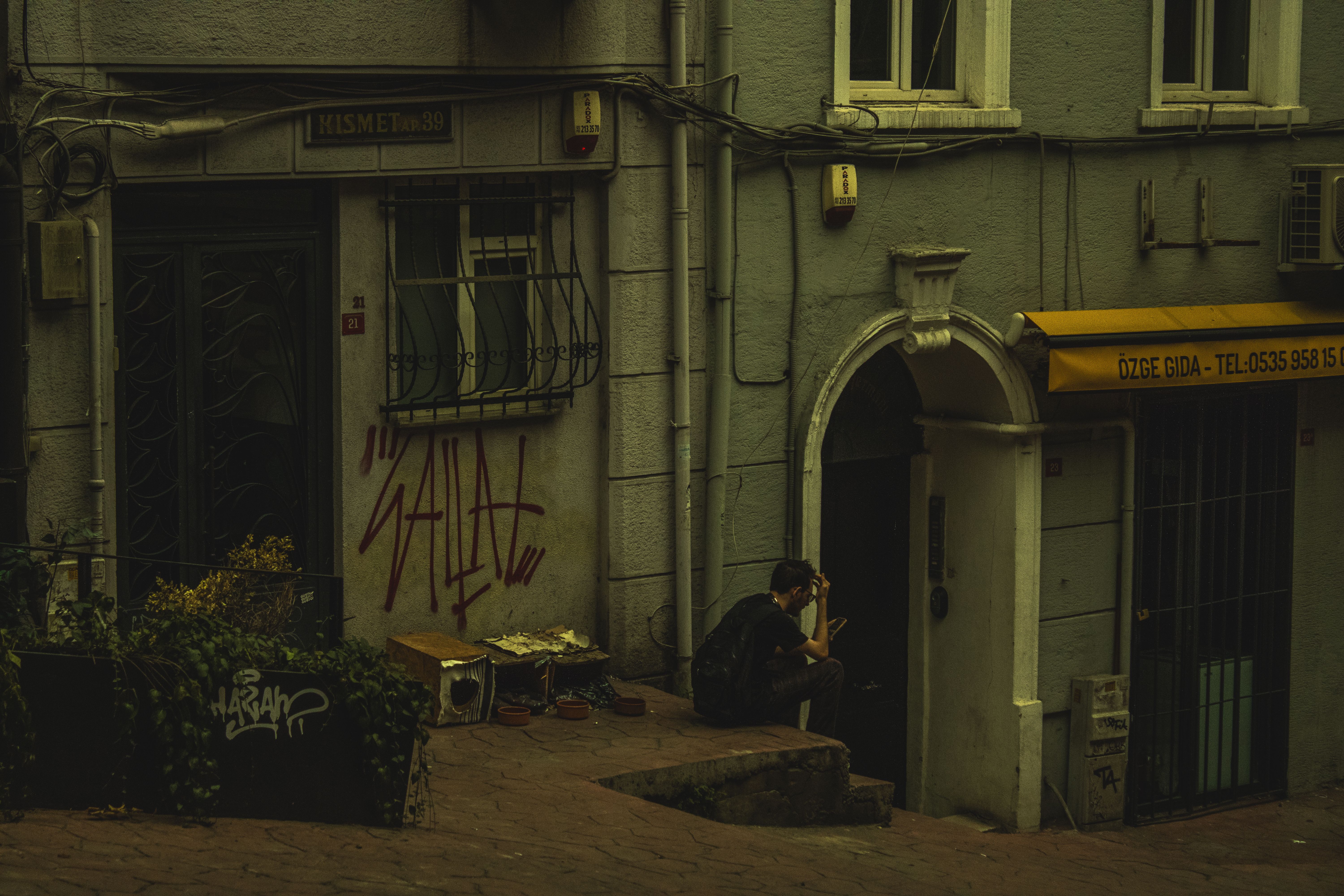 Man Sitting in an Alley with a Smartphone in Hand · Free Stock Photo