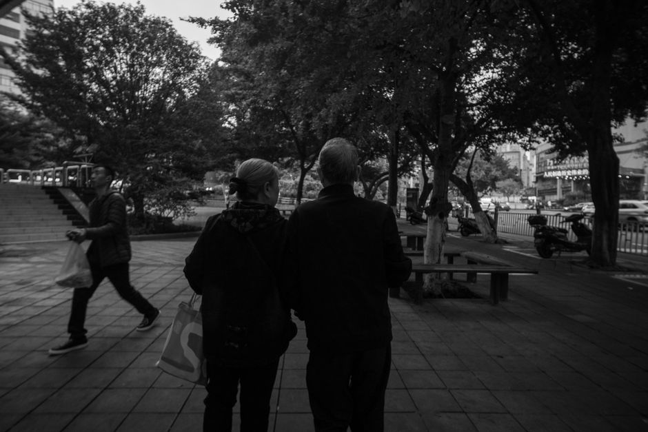 A couple walks hand in hand through a city park in black and white.