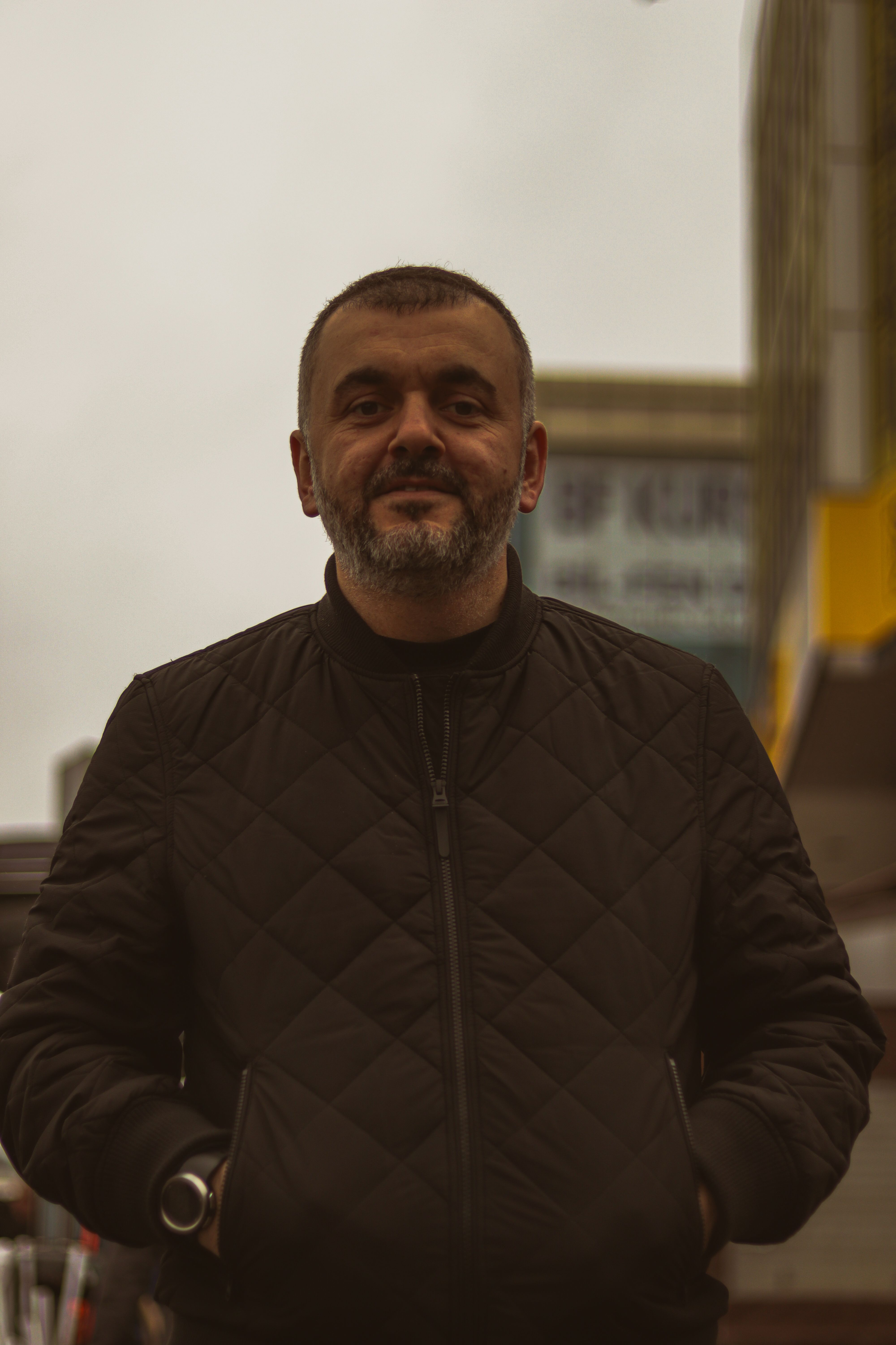 Portrait of a mature man in a quilted jacket standing confidently in an urban setting.