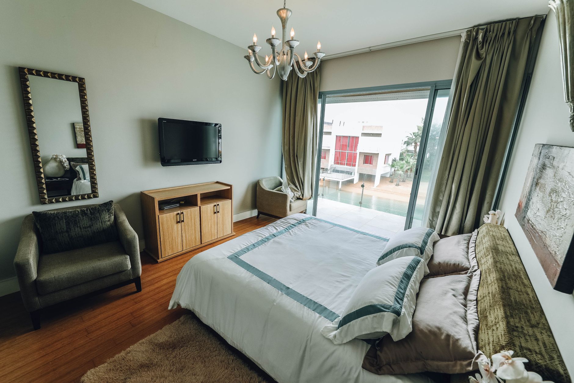 睡覺怕亮又怕黑?臥室光線層次這樣打造 Stylish contemporary bedroom featuring modern furniture, a chandelier, and natural lighting through sliding doors.
