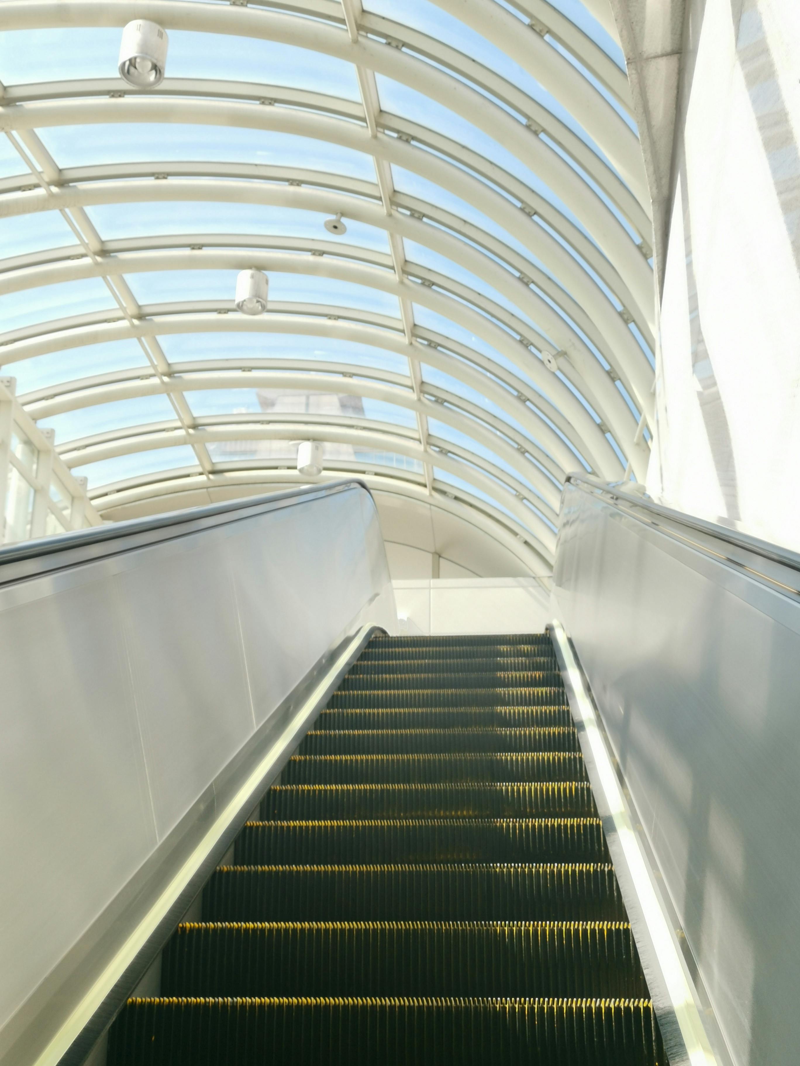 Upward view of a modern escalator with a glass arch roof in Taipei, Taiwan.