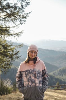 A young woman in a beanie and jacket smiles while hiking in a mountain forest.