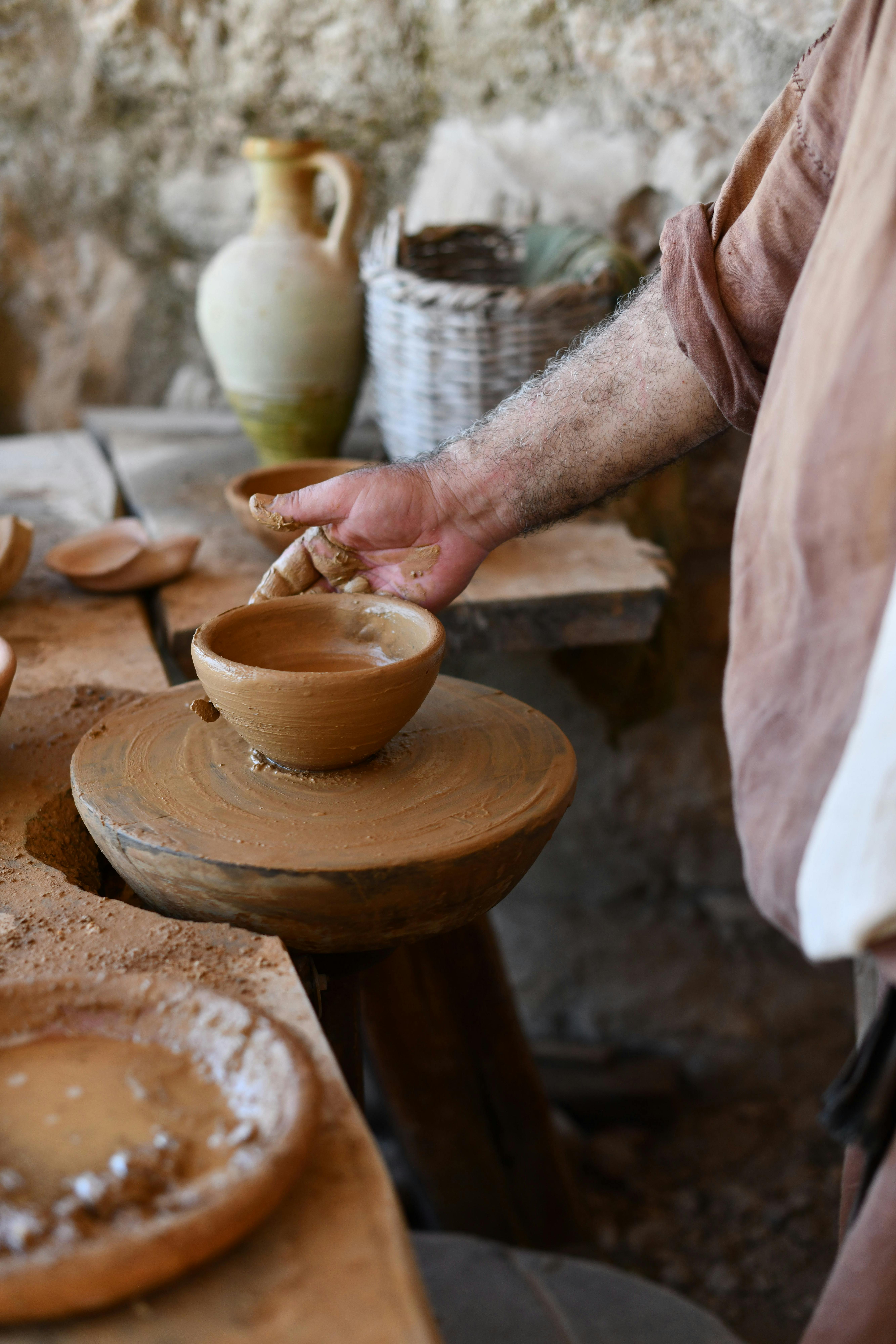 A skilled potter handcrafts a clay bowl, showcasing traditional pottery techniques in a rustic workshop.