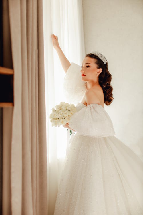 A bride in a wedding dress leaning against a window