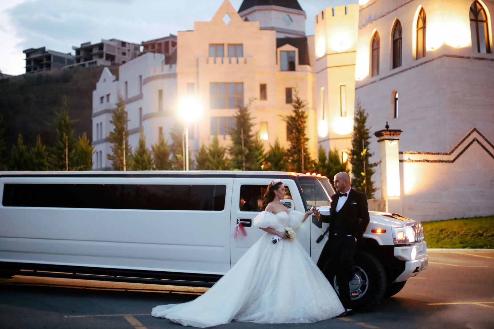 Illustrative photograph of newlyweds beside a limousine at an illuminated venue at night.