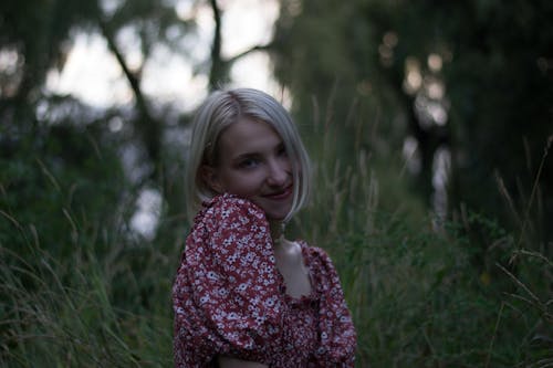 Young Woman in a Blouse with Floral Pattern Standing on a Meadow 