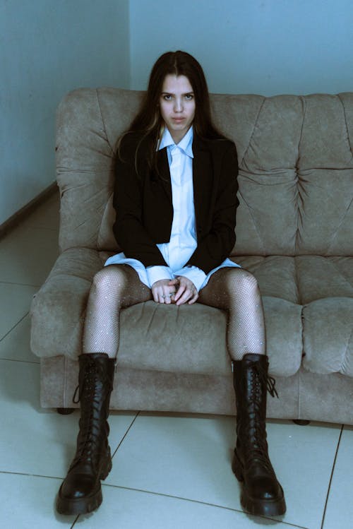 Young Woman Wearing a White Shirt, Black Jacket and Boots Sitting on a Sofa 