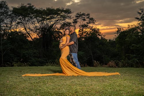 Man Hugging Pregnant Woman in Yellow Dress at Sunset