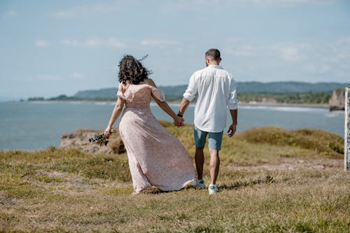 Woman in Dress and Man in White Shirt Walking on Coast