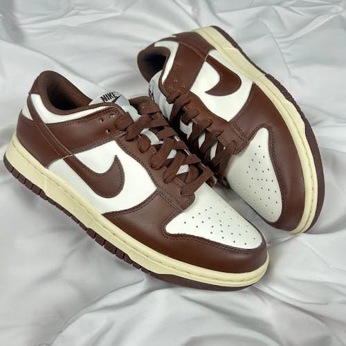 Free Stylish Nike Dunk Low sneakers in brown and white leather displayed on a white fabric. Stock Photo