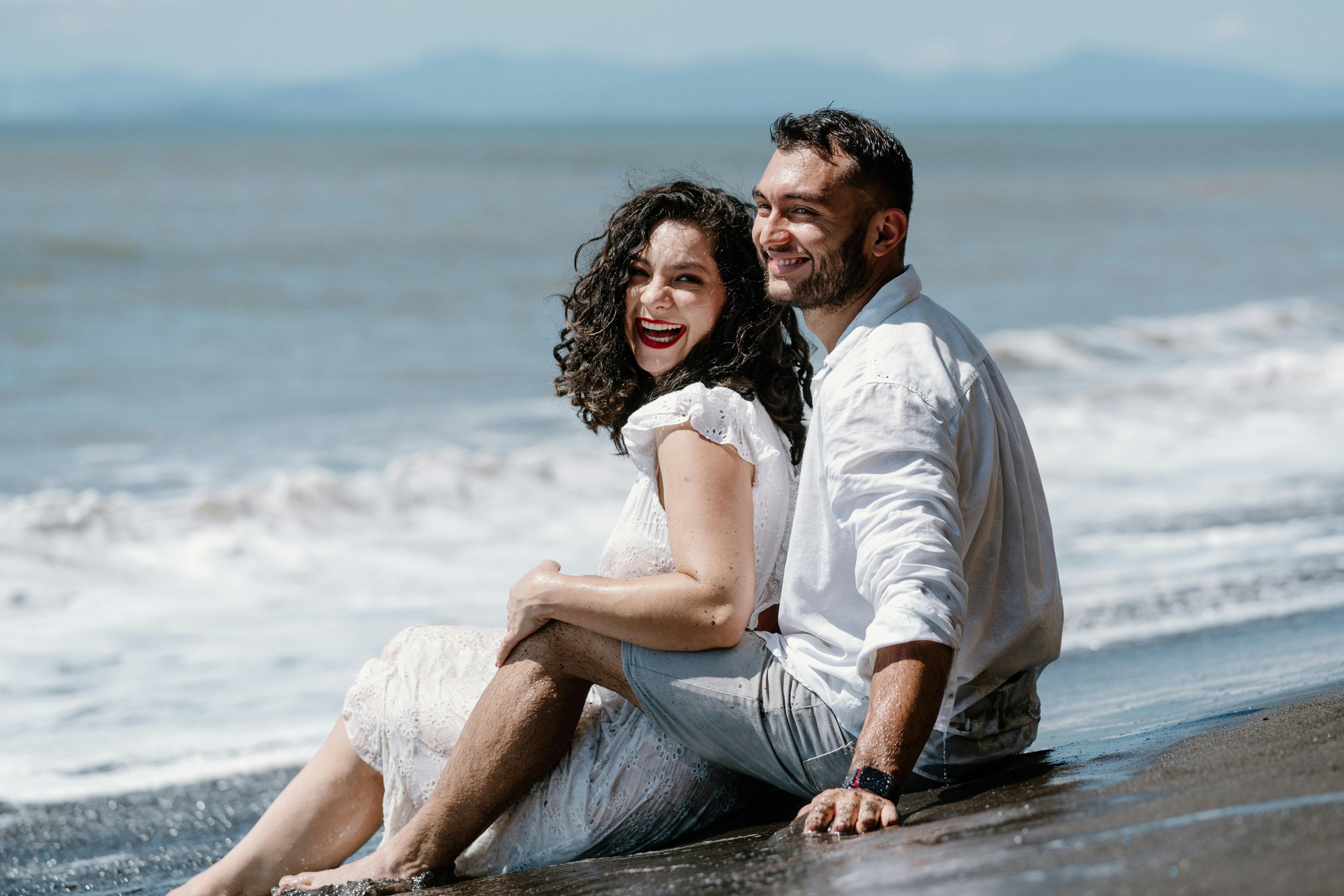 Free A Happy Couple Sitting on a Beach and Embracing Stock Photo