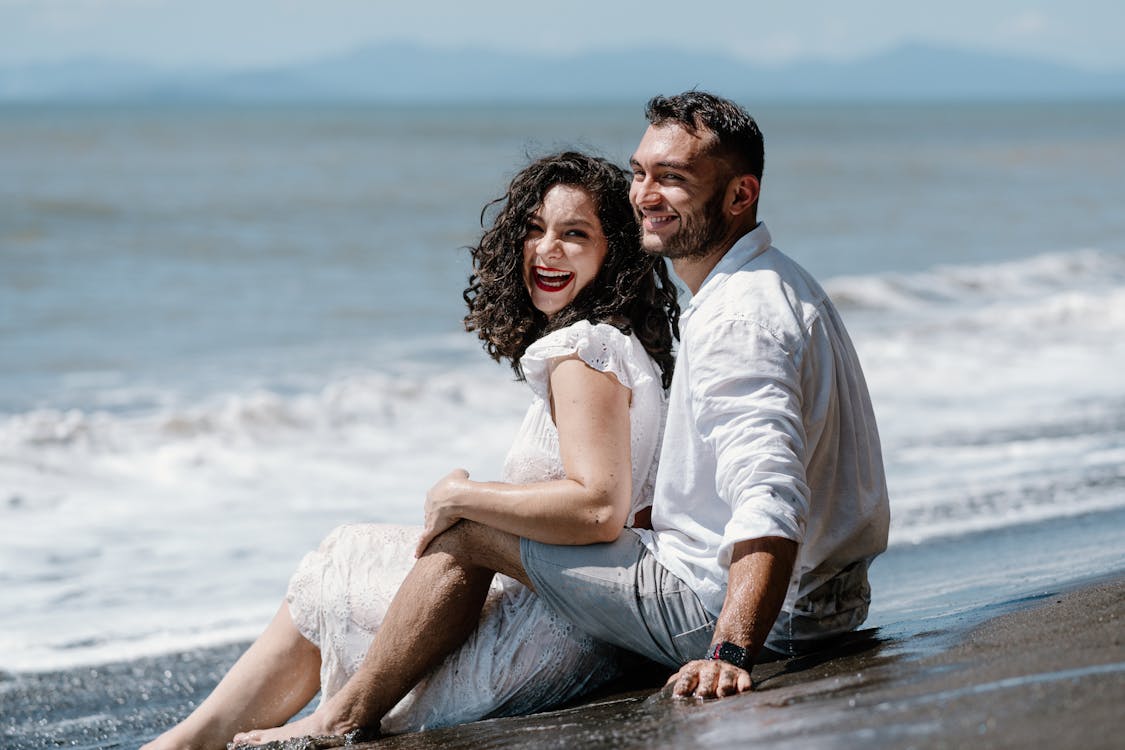 Free A Happy Couple Sitting on a Beach and Embracing Stock Photo