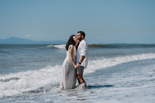 A couple standing in the ocean with waves crashing behind them