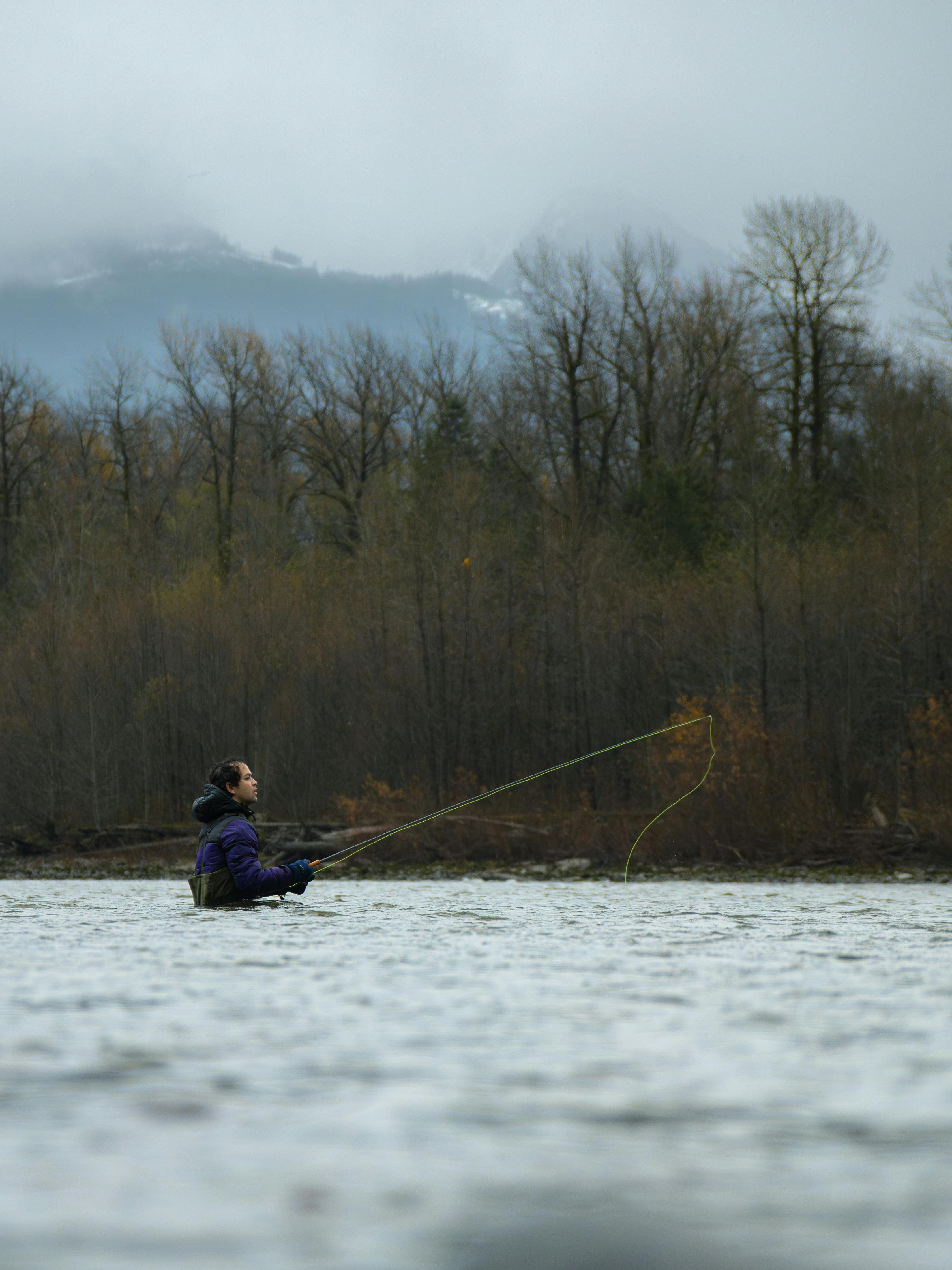 A man fly fishing in a peaceful river surrounded by autumn trees and mountains.