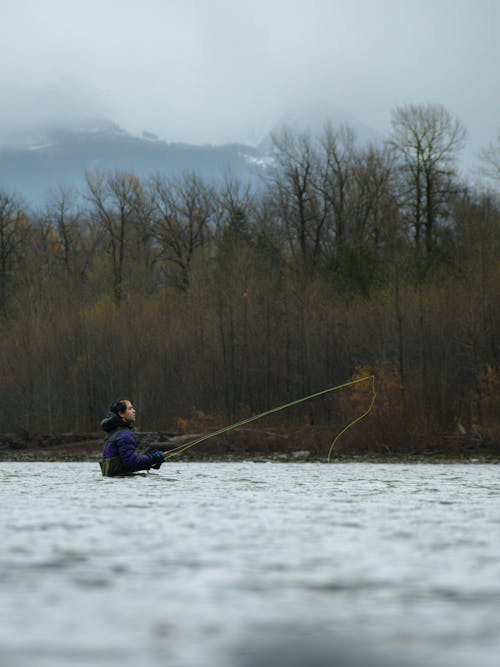 A man fly fishing in the water with a tree in the background