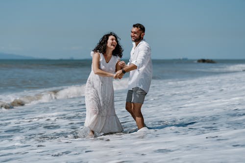 A couple in white dress and sandals walking in the ocean