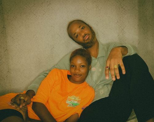 Free A couple lounging together indoors, wearing colorful clothing and rings, exuding a warm and intimate vibe. Stock Photo