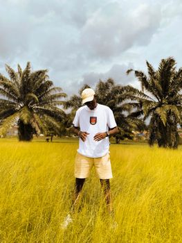 Stylish young man wearing sunglasses and white t-shirt stands in a tropical field in Ibadan, Nigeria.