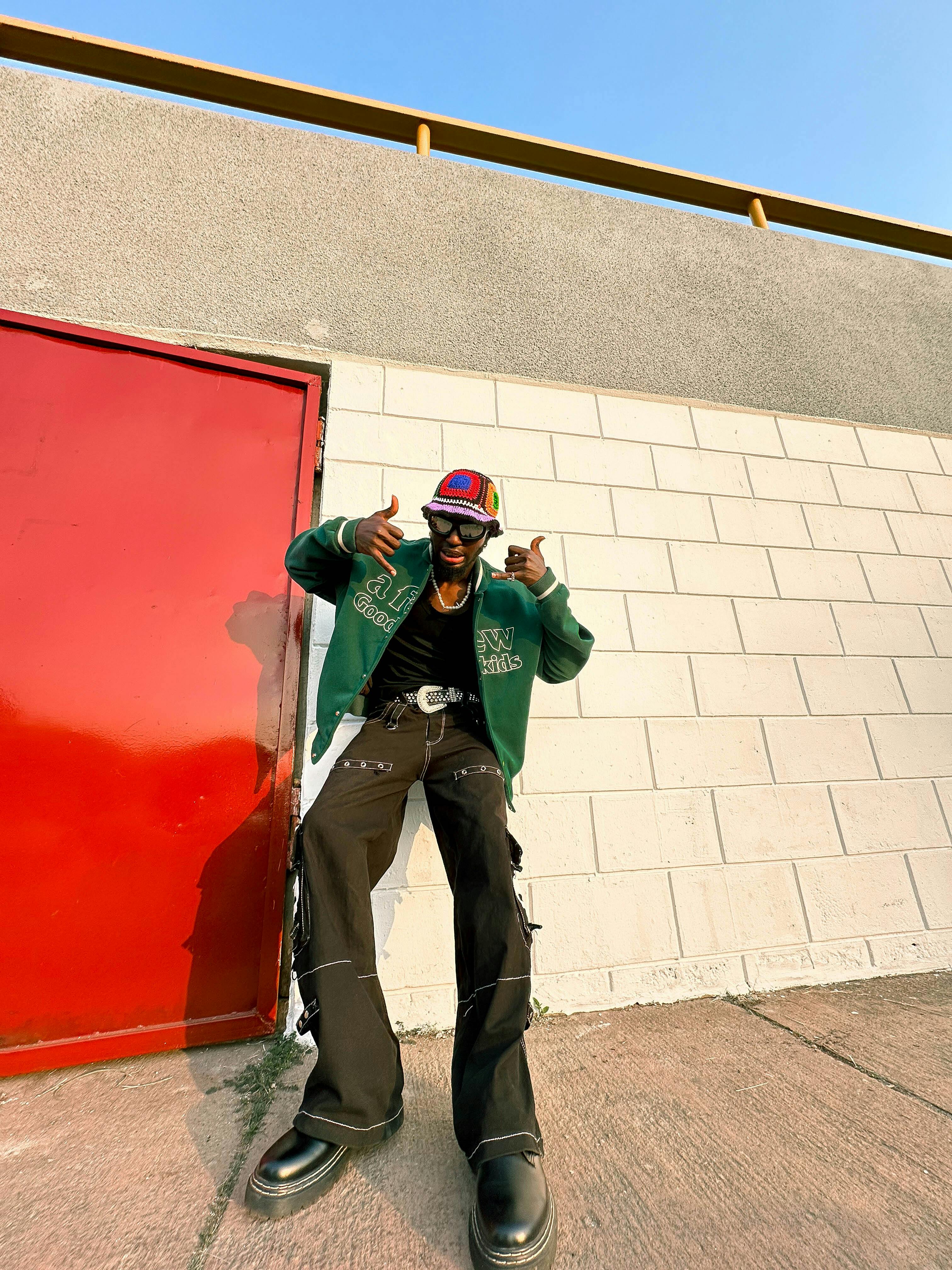 Fashionable young man posing by a red door in Ife, Nigeria, showcasing urban street style.