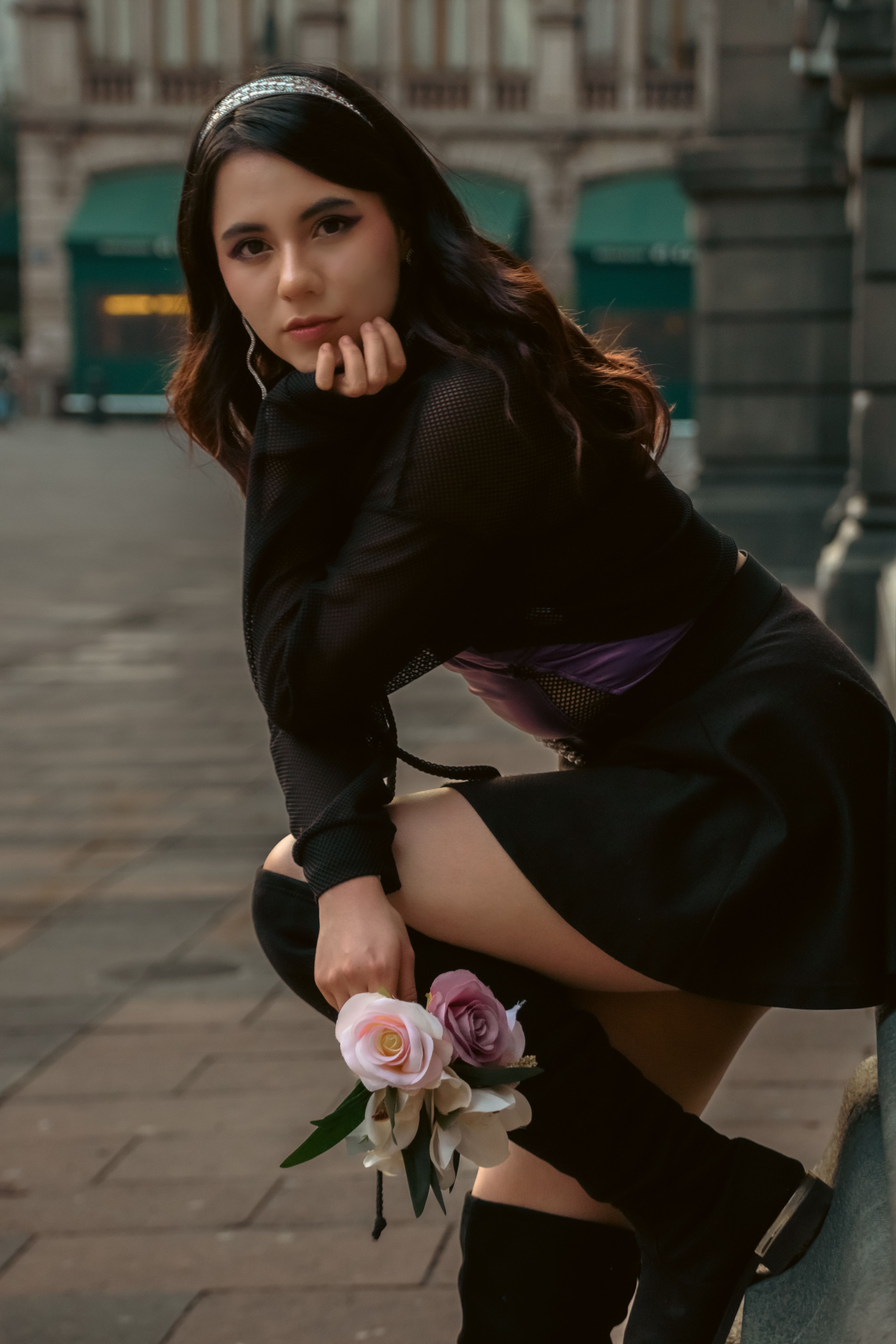 Chic woman in black attire posing with roses in an urban setting, exuding style and grace.