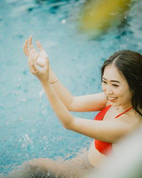 A smiling woman in a red bikini enjoys swimming in a pool during the warm summer day.