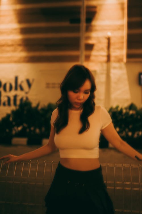 A woman in a crop top and skirt standing near a fence