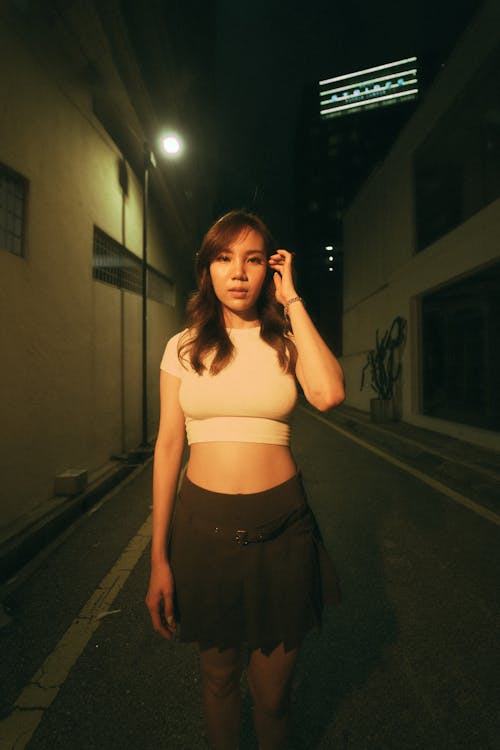 Young Woman in a Crop Top and Skirt Standing on a Street in City at Night 