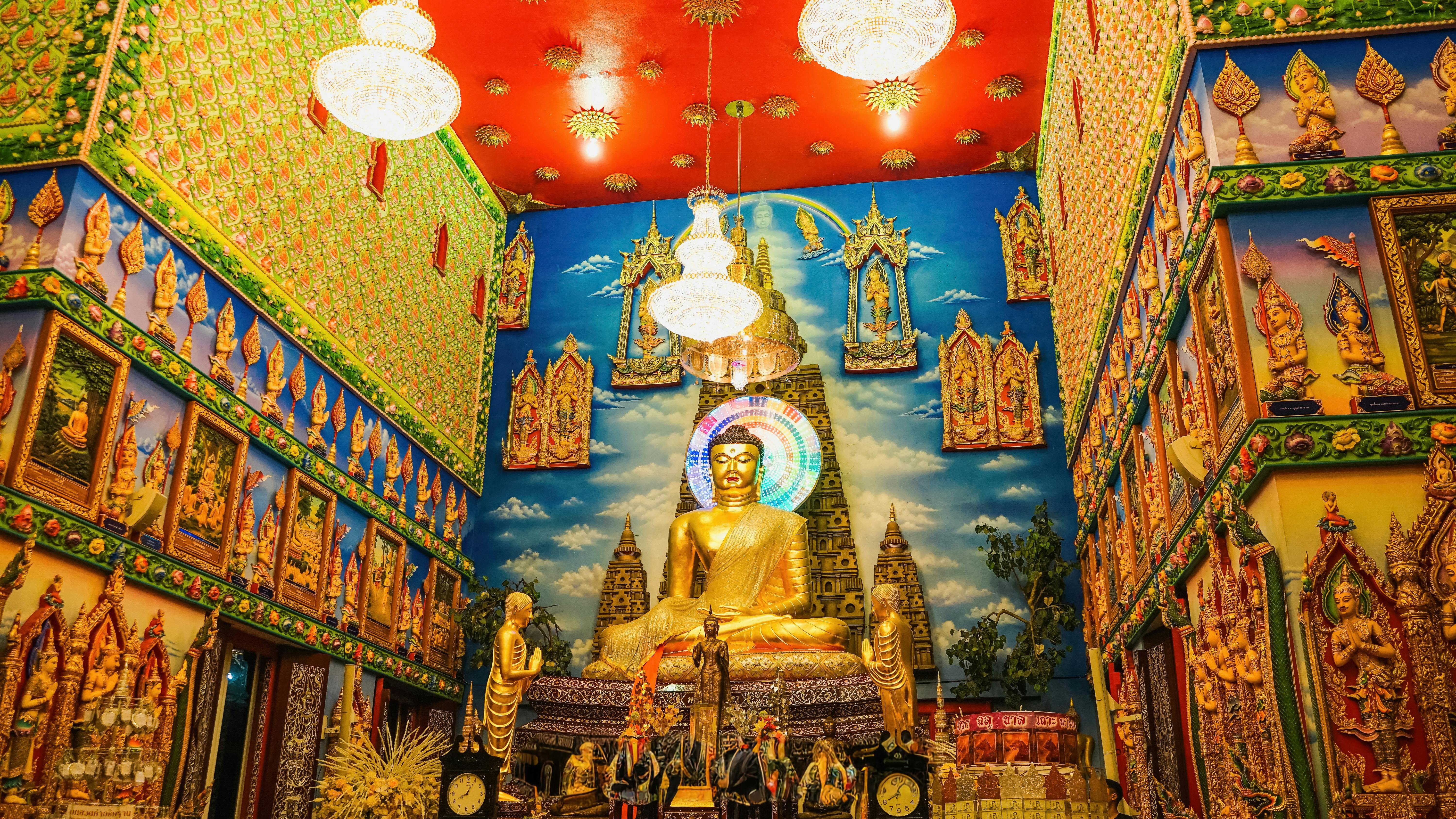 Vibrant interior featuring a golden Buddha statue amidst intricate art in a Thai temple.