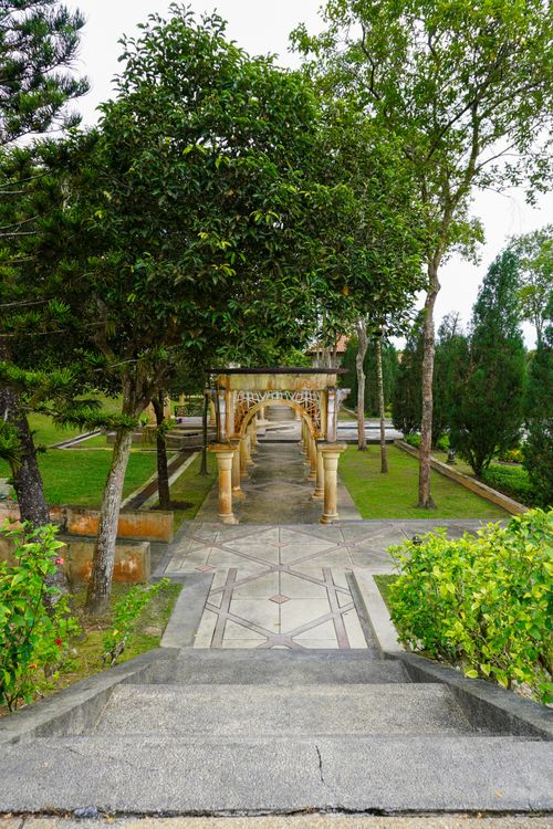 Free A serene garden featuring a stone colonnade surrounded by lush green trees and pathways. Stock Photo