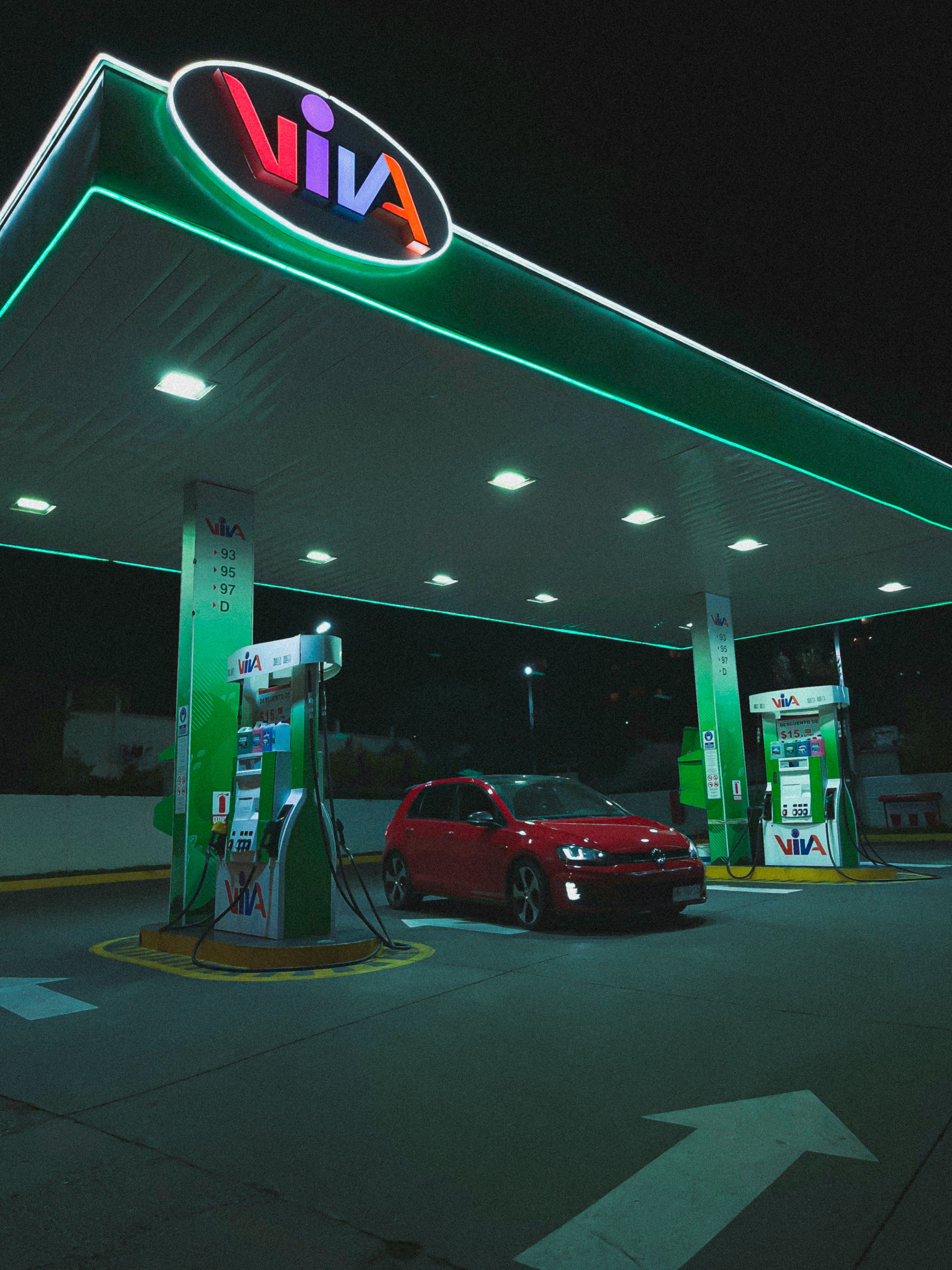 A red Volkswagen Golf parked under bright lights at a gas station at night.