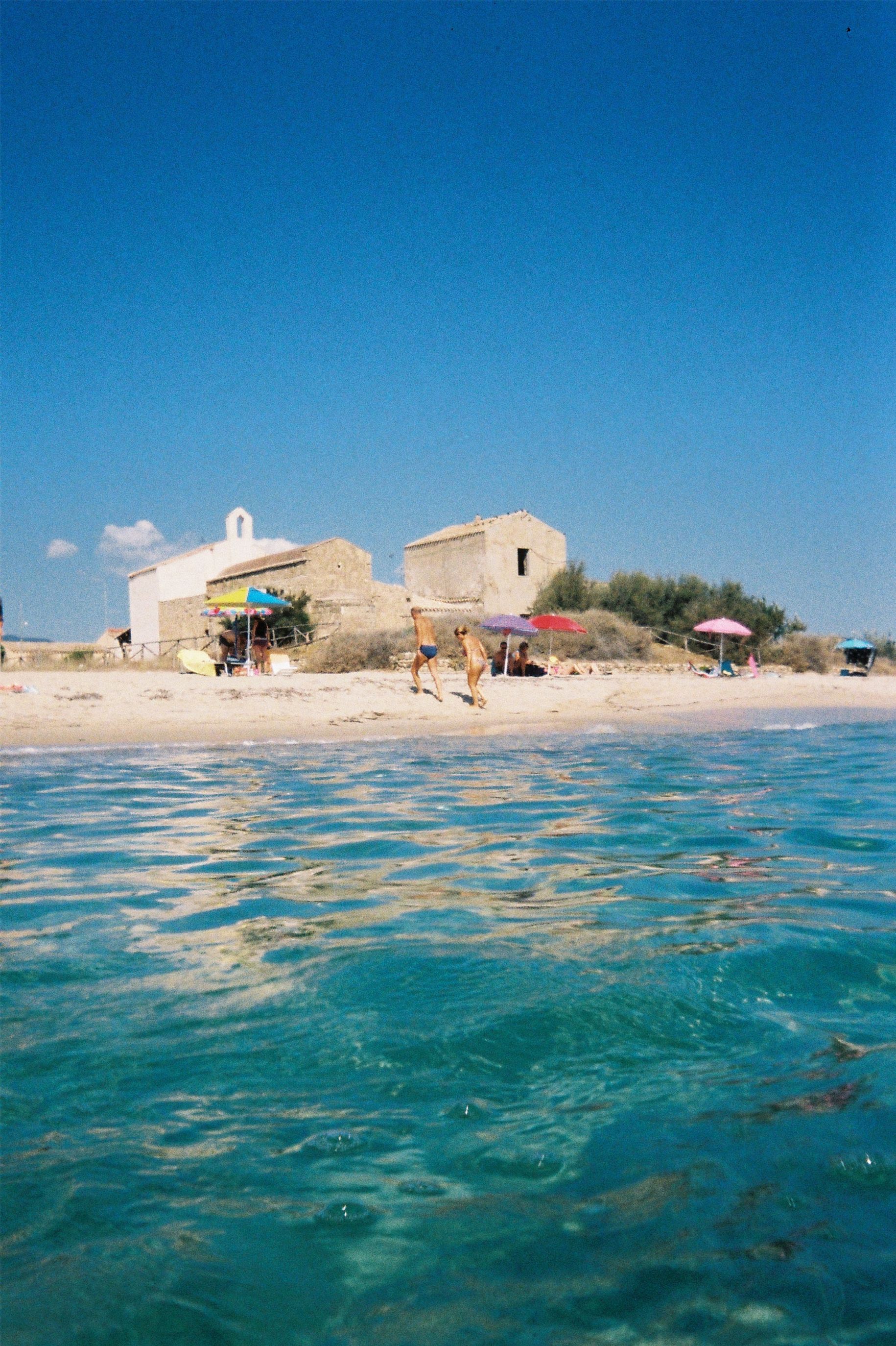 A serene Sardinian beach with rustic structures, vibrant umbrellas, and clear blue waters.