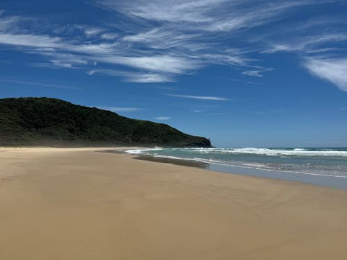 A sandy beach with a blue sky and clouds