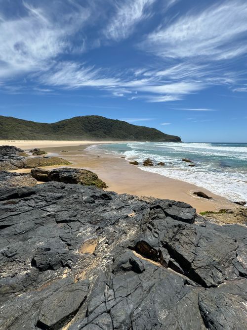 Free Beautiful rocky shoreline and sandy beach with vivid blue sky and rolling waves. Stock Photo