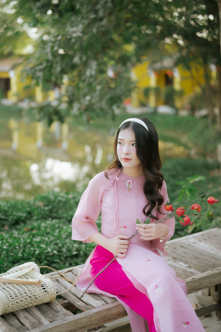 Young Woman In A Pink Ao Dai Dress Sitting In A Park 