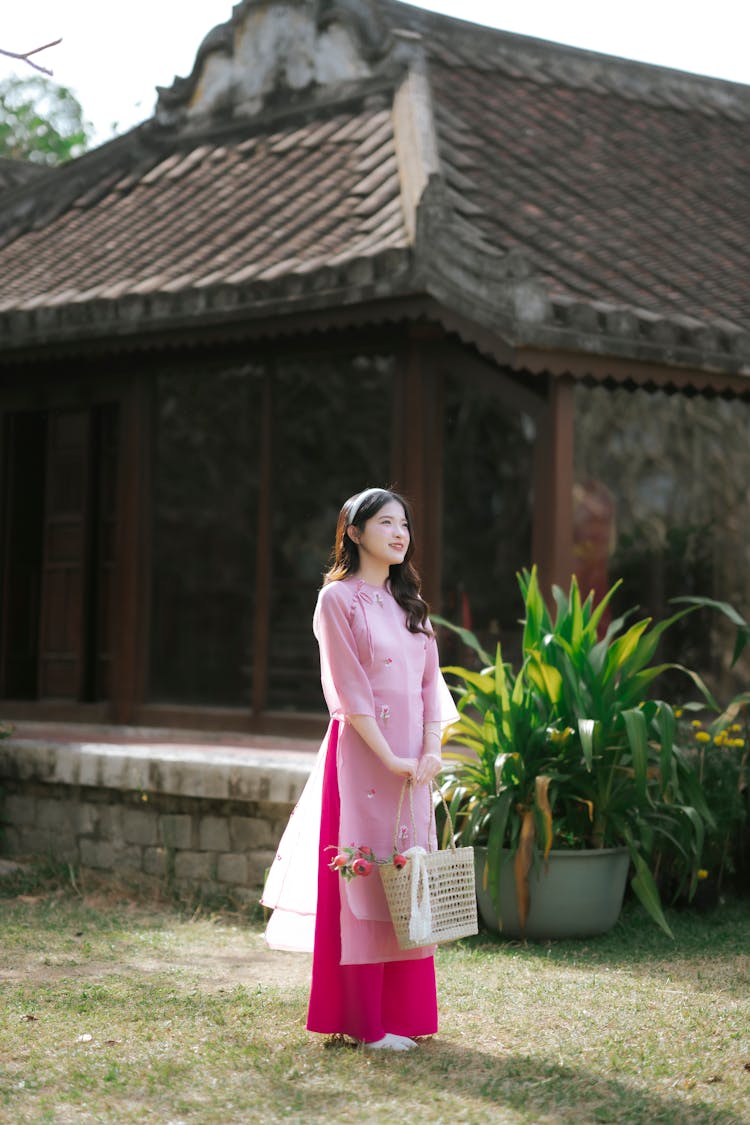 Young Woman In A Pink Ao Dai Dress Standing Near A Building 