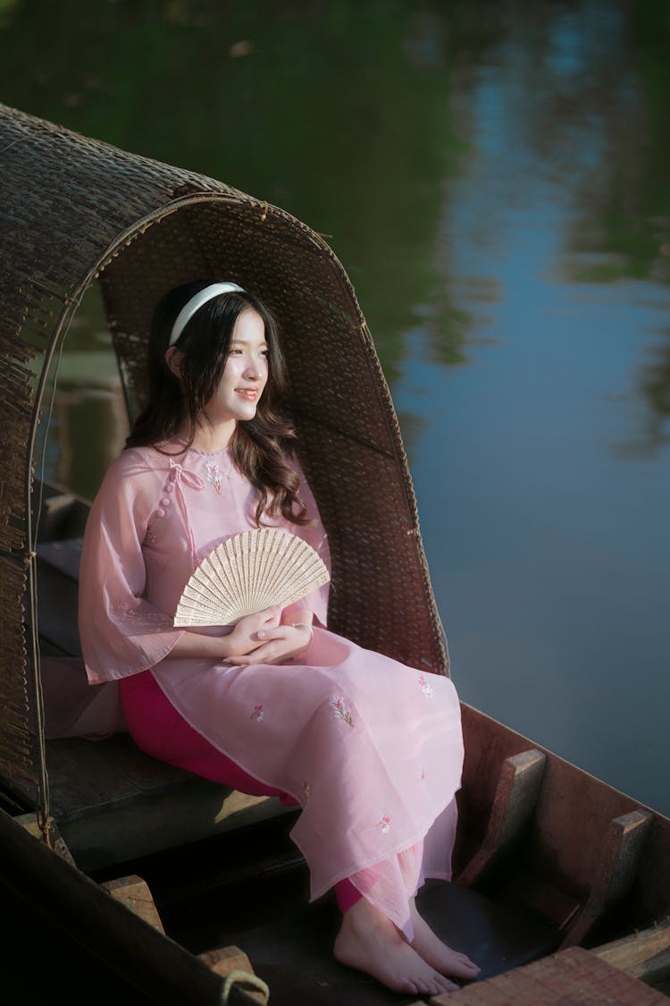 Young Woman In A Pink Ao Dai Dress Sitting On A Boat