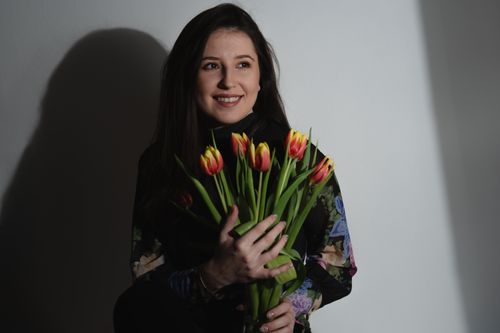 Free Smiling woman in a floral dress holds vibrant tulips, exuding warmth and joy in a studio setting. Stock Photo