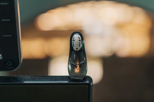 A close-up of an artistic figurine placed on the edge of a monitor with a blurred background.
